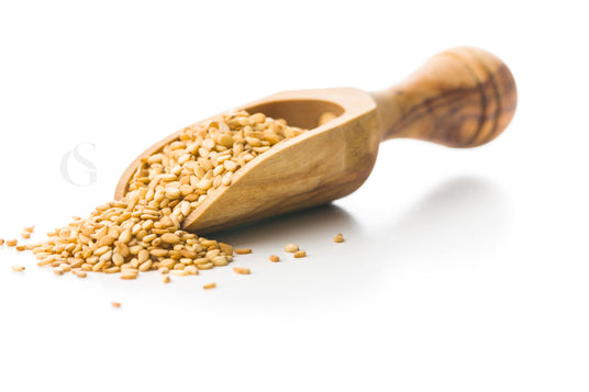 carved wooden hand scoop with light brown sesame seeds spilling out, white background