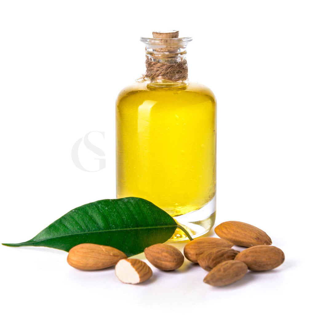 cylindrical glass bottle withe cork stopper and twine around stem and yellow liquid inside, green leaf and almonds in foreground, white background