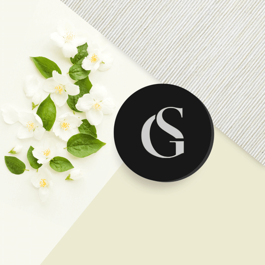 black round jar to the right with white flowers and green leaves on a background of white, cream and textured light grey
