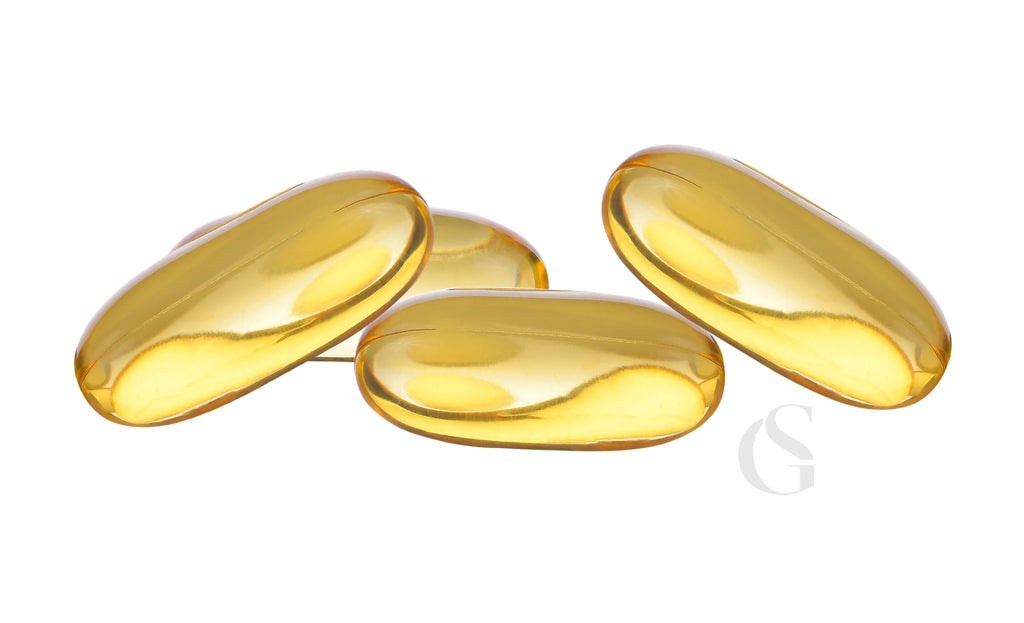 group of four oblong yellow soft-gel vitamins on white background