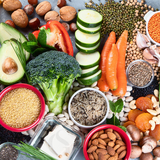 assortment of vegetables, grains, nuts, herbs, and dried fruits in dishes or on slate colored surface