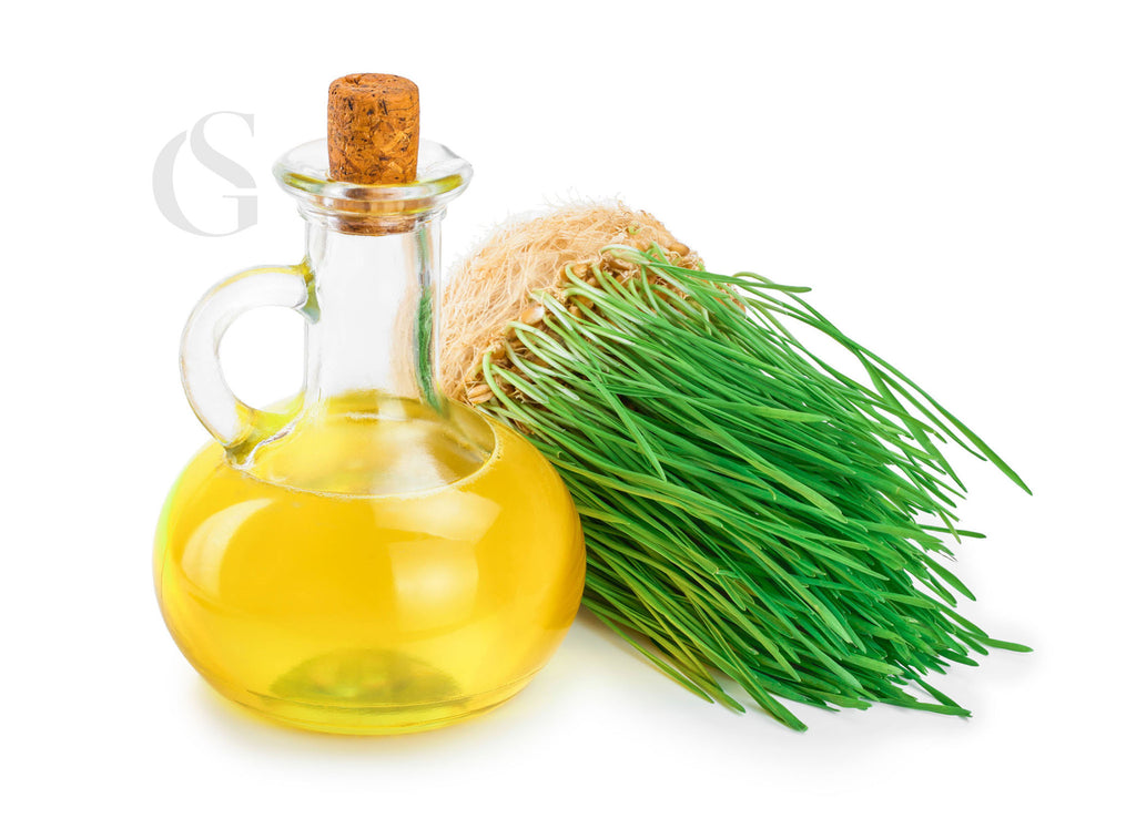 wide glass bottle with a small neck containing a cork stopper and circular handle containing golden oil next to a green wheat grass plant on its side