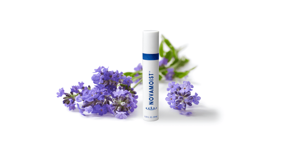 small cylindrical white and blue bottle in front of a small bouquet of purple flowers, white background 