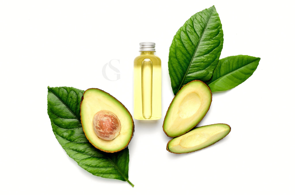 cut avocado sections in the peel with leaves behind and a small cylindrical bottle of pale yellow oil between