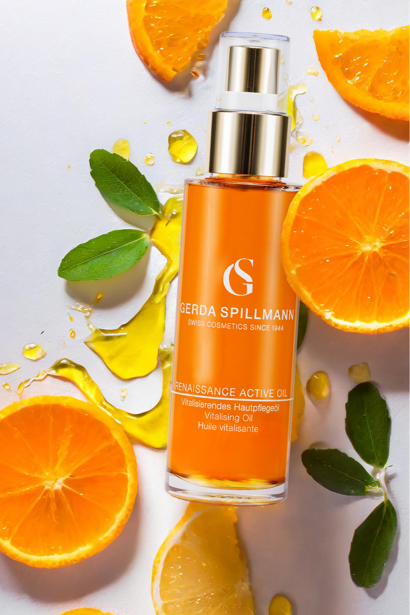 Orange skincare oil bottle with sliced oranges and leaves on a light background