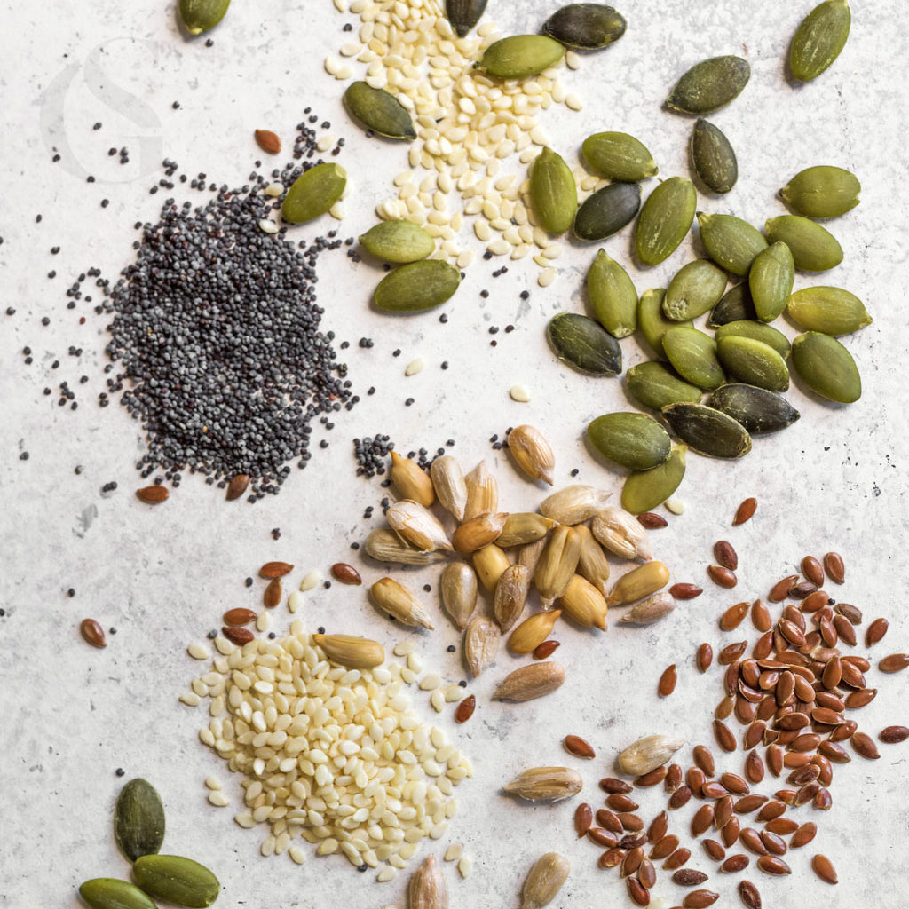 groups of seeds in varying colors and sizes loosely grouped on a white stone background